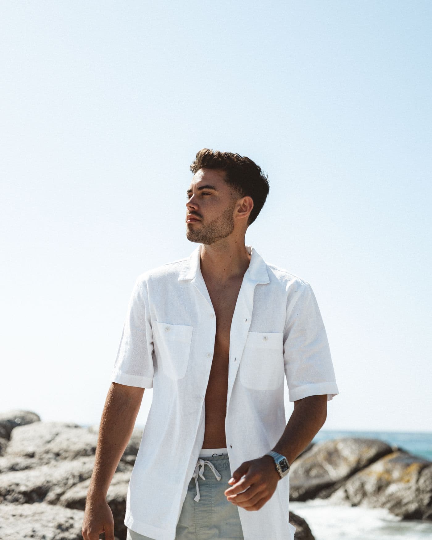 A man in an open white linen shirt by the sea