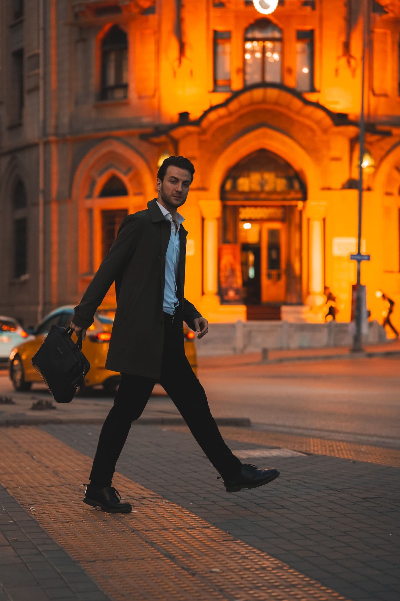 A man in a dark suit with a briefcase walking past a golden-lit building at dusk