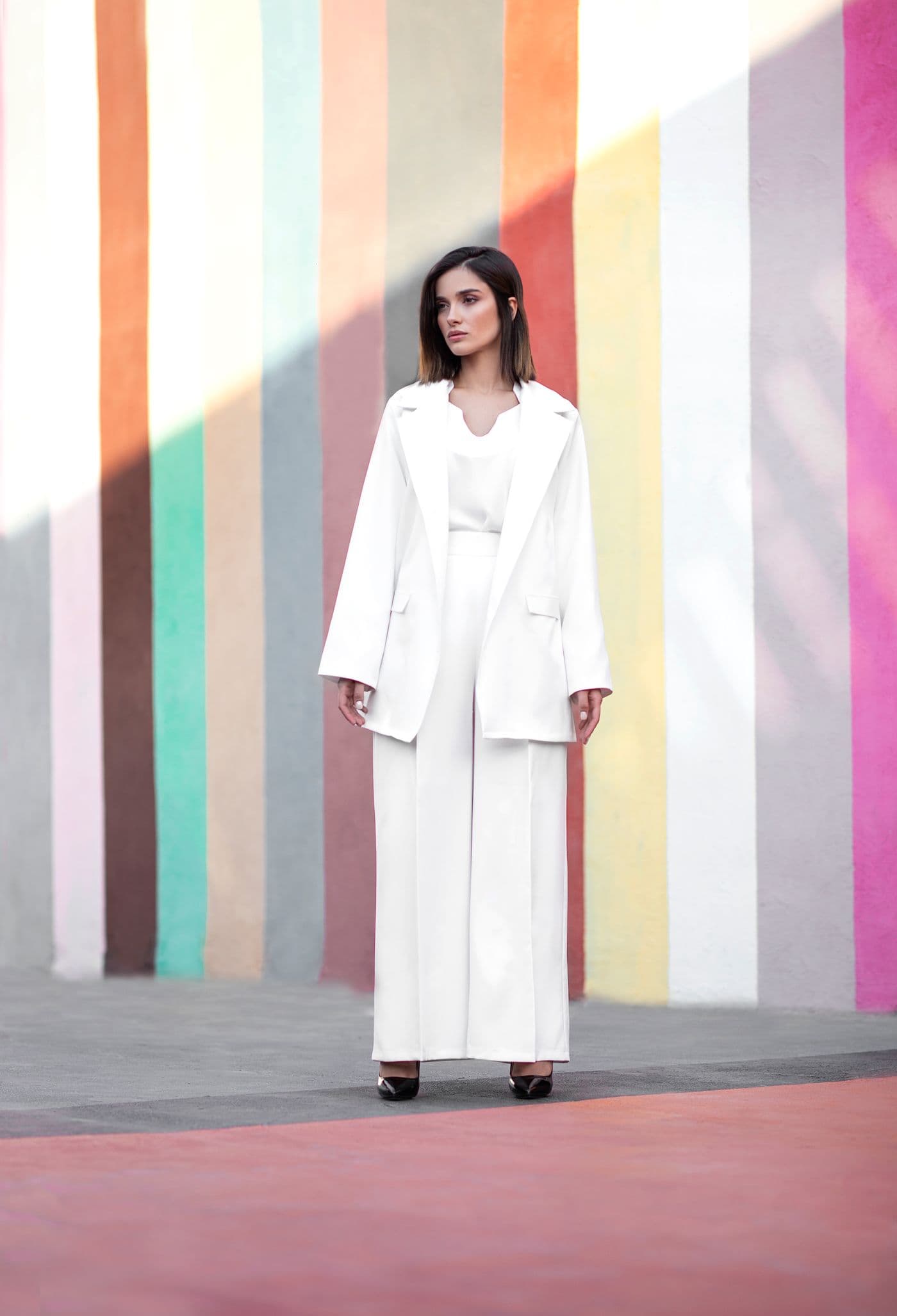 A woman in a tailored white suit in front of a softly striped art wall